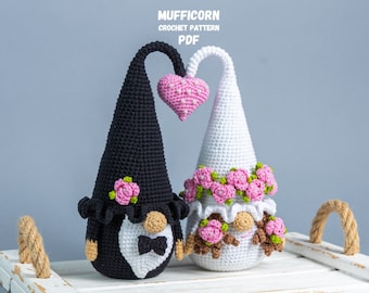 May include: Two crocheted gnomes, one black and one white, holding a pink heart. They are wearing flower crowns and the black gnome has a white bow tie. The gnomes are sitting on a white tray with rope handles. The text "MUFFICORN CROCHET PATTERN PDF" is at the top of the image.