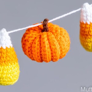 May include: A crocheted garland featuring orange pumpkins and yellow and orange candy corn decorations.