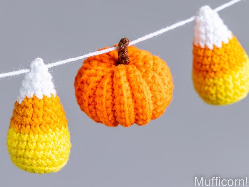 May include: A crocheted garland featuring orange pumpkins and yellow and orange candy corn decorations.