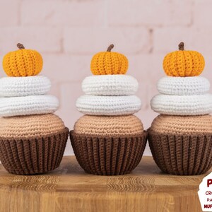 May include: Three crocheted pumpkin spice cupcakes with white frosting and orange pumpkins on top. The cupcakes are sitting on a wooden surface. The text "PDF CROCHET PATTERN MUFFICORN" is in the bottom right corner of the image.