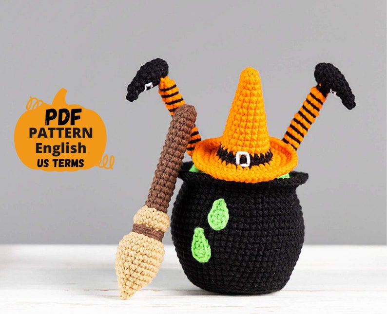 May include: Crocheted Halloween witch with a black cauldron, orange hat, and a brown and beige broom. The witch has orange and black striped legs and a black hat with a buckle. The text "PDF PATTERN English US TERMS" is on a pumpkin-shaped background.