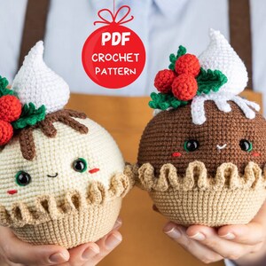 May include: Two crocheted Christmas pudding ornaments, one with white frosting and one with brown frosting. Both have a green holly sprig with red berries and a cute smiling face.