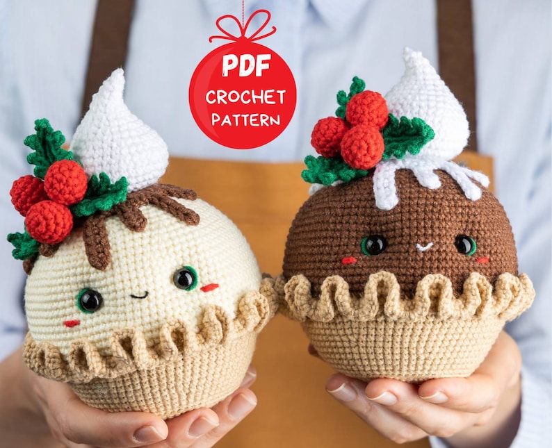 May include: Two crocheted Christmas pudding ornaments, one with white frosting and one with brown frosting. Both have a green holly sprig with red berries and a cute smiling face.