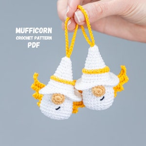 May include: Two white crocheted gnomes with yellow yarn hats and yellow yarn hair. The gnomes are hanging from yellow yarn loops. The text "MUFFICORN CROCHET PATTERN PDF" is visible in the image.