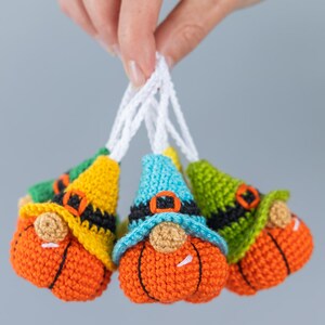 May include: Four crocheted gnome ornaments with pumpkin-shaped bodies, each with a different colored hat: green, yellow, blue, and green. The gnomes have white beards and black belts.