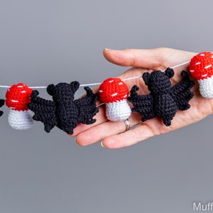 May include: A black and white crocheted garland with bats and mushrooms. The garland is strung on a white string and is hanging from a hand.