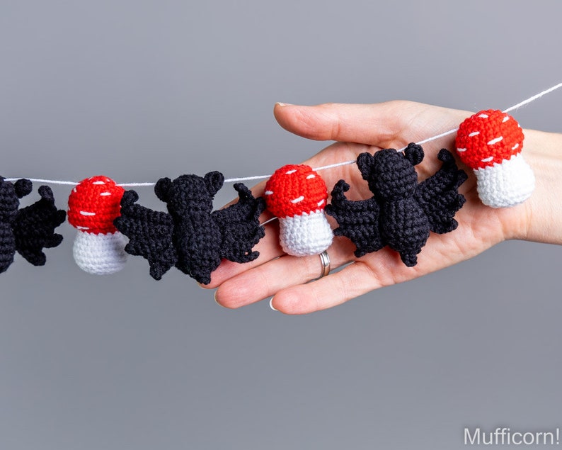 May include: A black and white crocheted garland with bats and mushrooms. The garland is strung on a white string and is hanging from a hand.