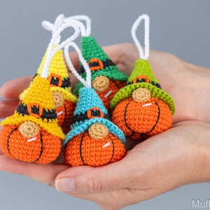 May include: Five crocheted pumpkin gnomes with different colored hats. The gnomes are orange with black eyes and a white nose. The hats are yellow, green, blue, and two shades of green.