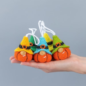 May include: Five crocheted pumpkin gnomes with different colored hats. The gnomes are orange with black eyes and a black belt. The hats are yellow, green, blue, and green.