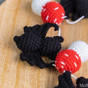 May include: A crocheted garland with alternating black bats and red and white mushrooms. The garland is strung together with white yarn.