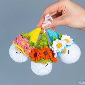 May include: Three crocheted gnome ornaments with white faces, black eyes, and red noses. Each gnome has a different colored hat with flowers: pink and yellow flowers, orange flowers, and white flowers.