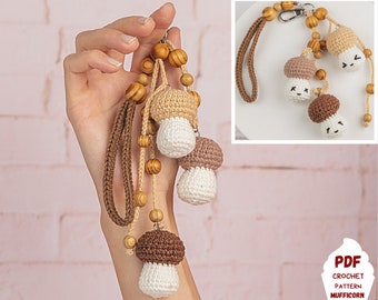 Può includere: Un portachiavi a forma di fungo all'uncinetto con filato marrone e bianco, perline di legno e un cinturino in pelle marrone. Il portachiavi è appeso a una mano. Il testo "PDF CROCHET PATTERN MUFFICORN" è nell'angolo in basso a destra dell'immagine.