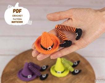 May include: Crochet pattern PDF for a witch leg ornament. The ornament is orange, black, and white. The witch leg is wearing a black shoe and has orange and black striped stockings. The witch leg is laying on a hand. The PDF is titled "PDF Crochet Pattern Mufficorn".