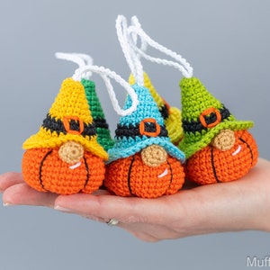 May include: Three crocheted pumpkin gnomes with different colored hats. The gnomes are wearing black belts and have orange pumpkin bodies. The hats are yellow, blue, and green.