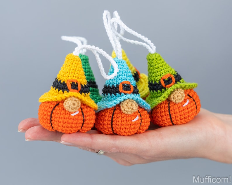 May include: Three crocheted pumpkin gnomes with different colored hats. The gnomes are wearing black belts and have orange pumpkin bodies. The hats are yellow, blue, and green.