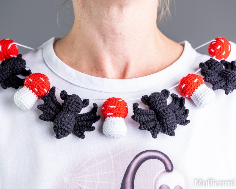 May include: A white shirt with a crocheted garland of black bats and red and white mushrooms. The garland is worn as a necklace.