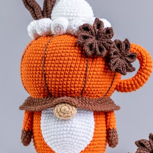 Puede incluir: Un gnomo con forma de calabaza naranja tejido a ganchillo, con barba y sombrero blancos, detalles marrones y un asa de taza. La calabaza est&aacute; adornada con an&iacute;s estrellado marr&oacute;n y una cobertura de crema batida blanca. Un art&iacute;culo decorativo con tem&aacute;tica oto&ntilde;al.