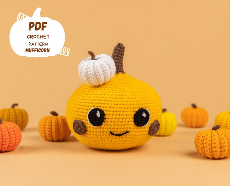 May include: A crocheted pumpkin with a smiling face and a white crocheted stem. The pumpkin is surrounded by smaller crocheted pumpkins in various shades of orange.