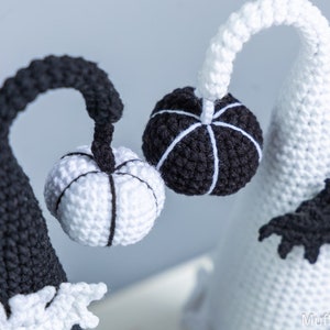 May include: Two crocheted Halloween gnomes with black and white striped pumpkins. The gnome on the left is black with a white pumpkin and the gnome on the right is white with a black pumpkin.