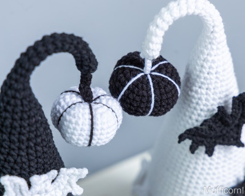May include: Two crocheted Halloween gnomes with black and white striped pumpkins. The gnome on the left is black with a white pumpkin and the gnome on the right is white with a black pumpkin.