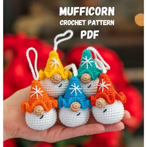 Op de afbeelding: Een verzameling van zes gehaakte kabouterornamenten in verschillende kleuren, waaronder oranje, geel, blauw en turquoise. Elke kabouter heeft een wit lichaam, een puntmuts met een sneeuwvlokontwerp en een kleine, ronde neus. De tekst "MUFFICORN CROCHET PATTERN PDF" is zichtbaar.