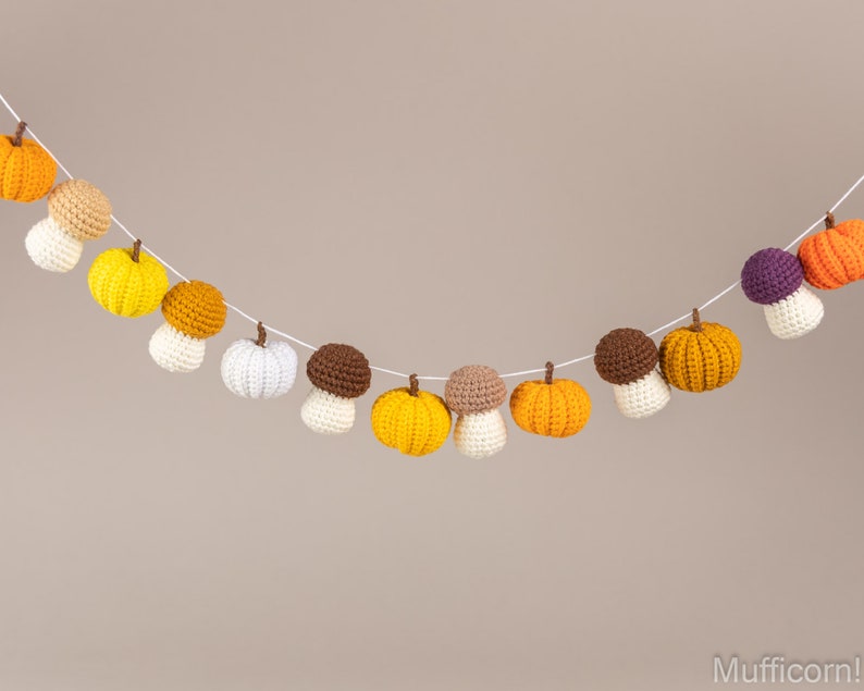May include: A garland of crocheted pumpkins and mushrooms in shades of orange, yellow, white, brown, and purple. The garland is strung on white twine and is perfect for fall decor.