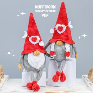 Pode incluir: Dois gnomos de crochê usando chapéus vermelhos com corações e flechas. Os gnomos estão sentados em blocos brancos. O texto "MUFFICORN CROCHET PATTERN PDF" está no topo da imagem.