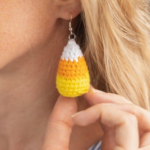 May include: Crocheted candy corn earrings in yellow, orange and white. The earrings are hanging from silver ear wires.