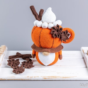 Puede incluir: Mu&ntilde;eca de gnomo de latte de especias de calabaza tejida a ganchillo con sombrero blanco, bufanda marr&oacute;n y detalles de an&iacute;s estrellado. La mu&ntilde;eca es naranja, marr&oacute;n y blanca, sobre una bandeja blanca.