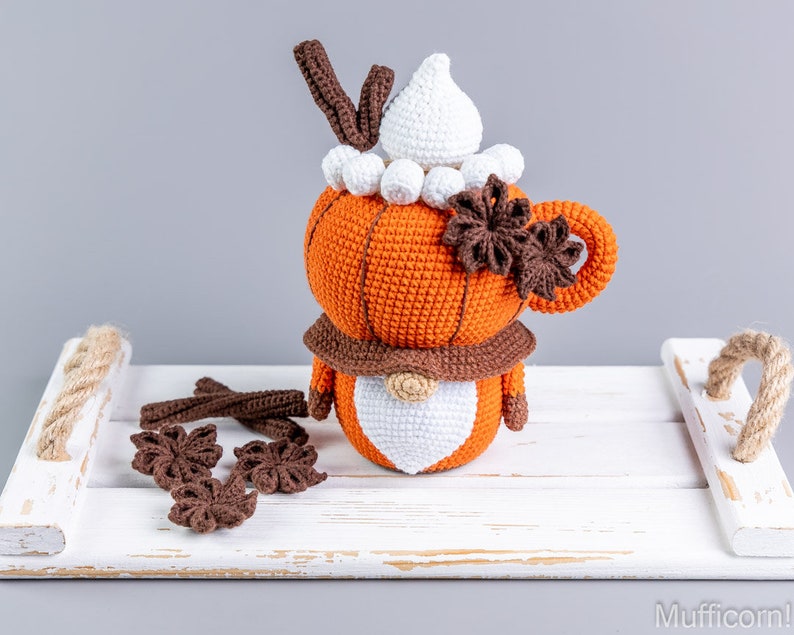Puede incluir: Mu&ntilde;eca de gnomo de latte de especias de calabaza tejida a ganchillo con sombrero blanco, bufanda marr&oacute;n y detalles de an&iacute;s estrellado. La mu&ntilde;eca es naranja, marr&oacute;n y blanca, sobre una bandeja blanca.