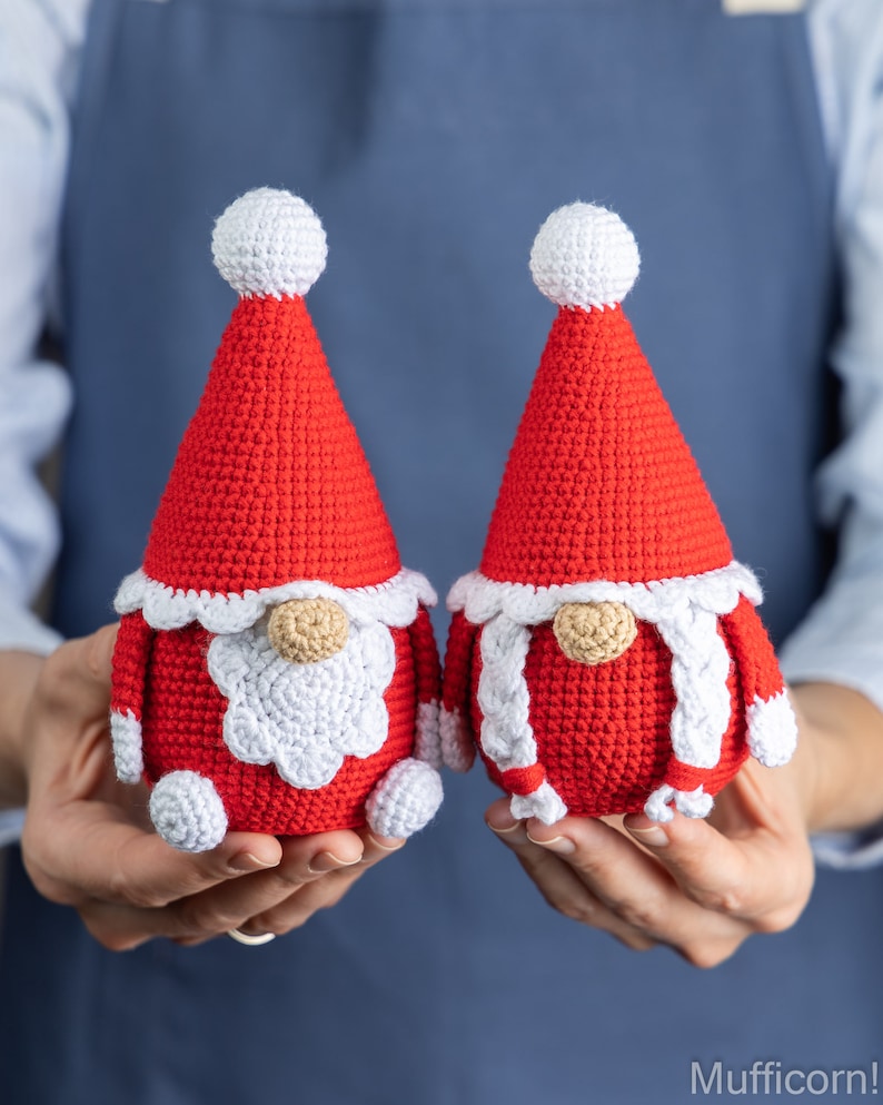 May include: Two crocheted gnomes in red and white, with white pom-poms on their hats. The gnomes are holding hands and have white beards and braids.