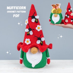Puede incluir: Patrón de crochet para un gnomo con un gorro rojo, flores blancas y abejas. El gnomo sostiene una maceta verde con una barba blanca. El patrón se llama "Mufficorn Crochet Pattern PDF".