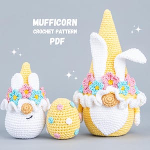 Könnte beinhalten: Ein Häkelmuster für die Herstellung eines Mufficorns, einer gnomartigen Figur mit einem Einhornhorn und einer Blumenkrone. Das Muster ist als PDF-Download erhältlich. Das Bild zeigt drei gehäkelte Figuren: ein großes Mufficorn aus gelbem und weißem Garn, ein kleineres Mufficorn aus weißem Garn und ein gelbes Ei.