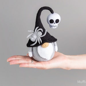 May include: A gray and black crocheted gnome wearing a black witch hat with a skull on top and a spider on the side.