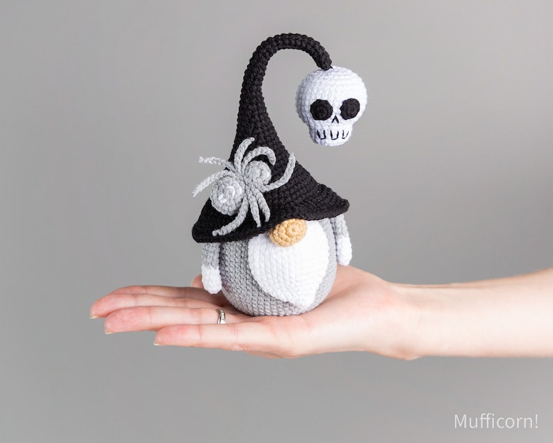 May include: A gray and black crocheted gnome wearing a black witch hat with a skull on top and a spider on the side.