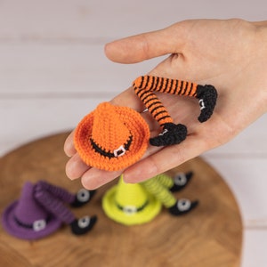 May include: Three crocheted witch leg ornaments with hats. The hats are orange, purple, and green. The legs are striped black and orange.