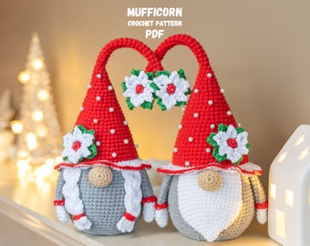 May include: Two red and white crocheted gnomes with white poinsettia flowers on their hats. The gnomes are standing on a shelf with a white house and a Christmas tree in the background. The text "MUFFICORN CROCHET PATTERN PDF" is at the top of the image.