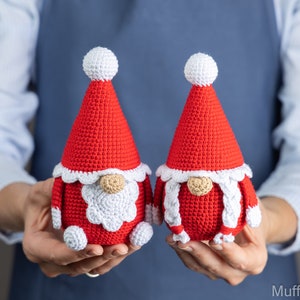 May include: Two crocheted gnomes wearing red hats with white trim and white beards. The gnomes are holding hands and are made of red and white yarn.