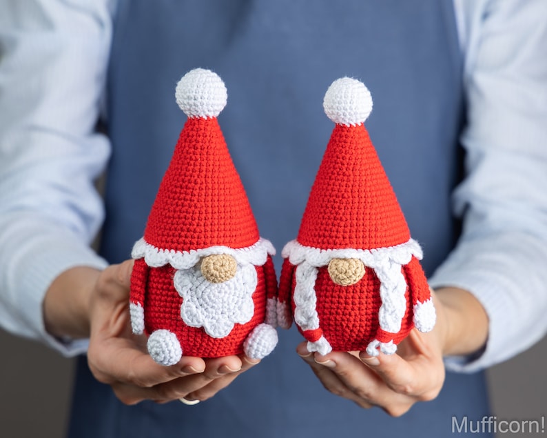 May include: Two crocheted gnomes wearing red hats with white trim and white beards. The gnomes are holding hands and are made of red and white yarn.