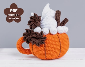 May include: A crocheted pumpkin mug with a white whipped cream topping, brown cinnamon sticks, and brown crocheted leaves.
