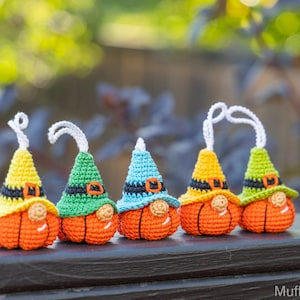 May include: Five crocheted pumpkin gnomes with different colored hats. The gnomes are orange with black eyes and noses. The hats are yellow, green, blue, yellow, and green.