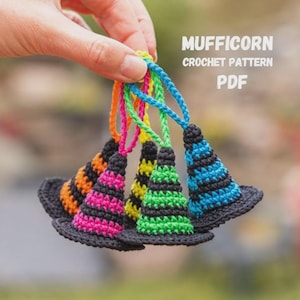 Könnte beinhalten: Eine Sammlung von fünf gehäkelten Miniatur-Hexenhüten in Orange, Pink, Gelb, Grün und Blau, jeweils mit schwarzen Streifen und einer passenden Aufhängeschlaufe. Der Text MUFFICORN CROCHET PATTERN PDF ist oben rechts zu sehen.