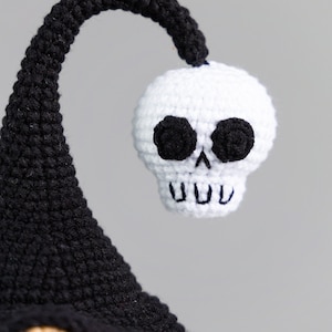 May include: A crocheted gnome with a black hat and a white skull on top. The skull has black eyes and a toothy grin.