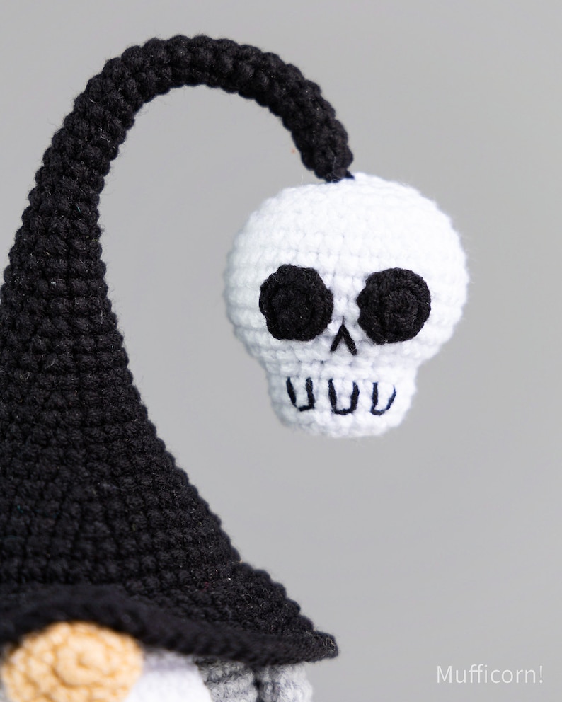 May include: A crocheted gnome with a black hat and a white skull on top. The skull has black eyes and a toothy grin.