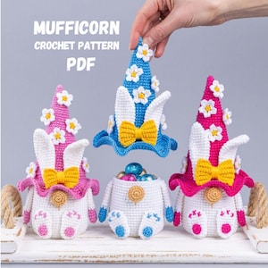Może przedstawiać: Szydełkowe figurki wielkanocnych gnomów w kolorze białym, różowym i niebieskim z uszami królika, żółtymi kokardkami i akcentami stokrotek. Figurki są prezentowane na białej tacy. Obraz zawiera tekst "MUFFICORN CROCHET PATTERN PDF".
