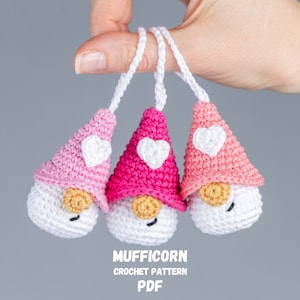 May include: Three handmade crochet gnomes in shades of pink and white, each with a heart-shaped accent on the hat. The gnomes have white bodies, tan noses, and black eyes. The text "MUFFICORN CROCHET PATTERN PDF" is visible.