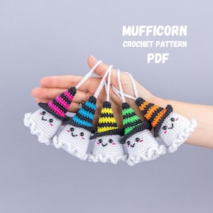 May include: Crocheted ghost ornaments with colorful witch hats. Each ghost has a smiling face and a white body with a ruffled edge. The hats are striped in pink, blue, yellow, green, and orange. The text "MUFFICORN CROCHET PATTERN PDF" is visible.