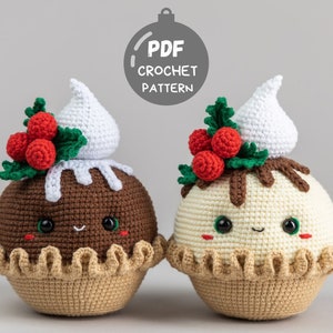 May include: Two crocheted Christmas pudding ornaments with cute faces. One is brown with white frosting and the other is white with brown frosting. Both have red holly berries and green leaves.