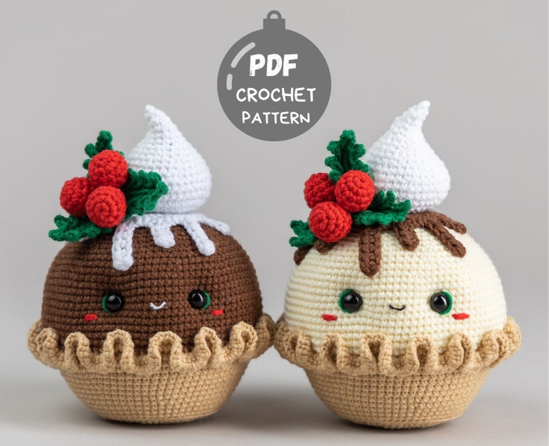 May include: Two crocheted Christmas pudding ornaments with cute faces. One is brown with white frosting and the other is white with brown frosting. Both have red holly berries and green leaves.