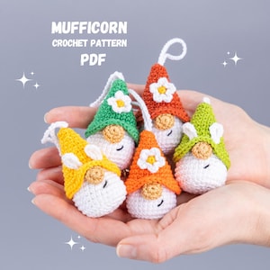 Puede incluir: Cinco gnomos de crochet con sombreros de diferentes colores. Los gnomos llevan caras blancas con ojos y bocas negras. Los sombreros son verdes, naranjas, amarillos y dos son naranjas. Los gnomos están sentados en la mano de una persona. El texto "MUFFICORN CROCHET PATTERN PDF" está en la parte superior de la imagen.